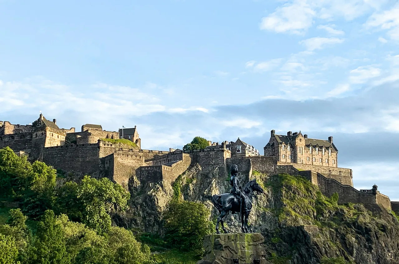 Edinburgh Castle on volcanic rock with an equestrian statue in the foreground and     green summer trees below