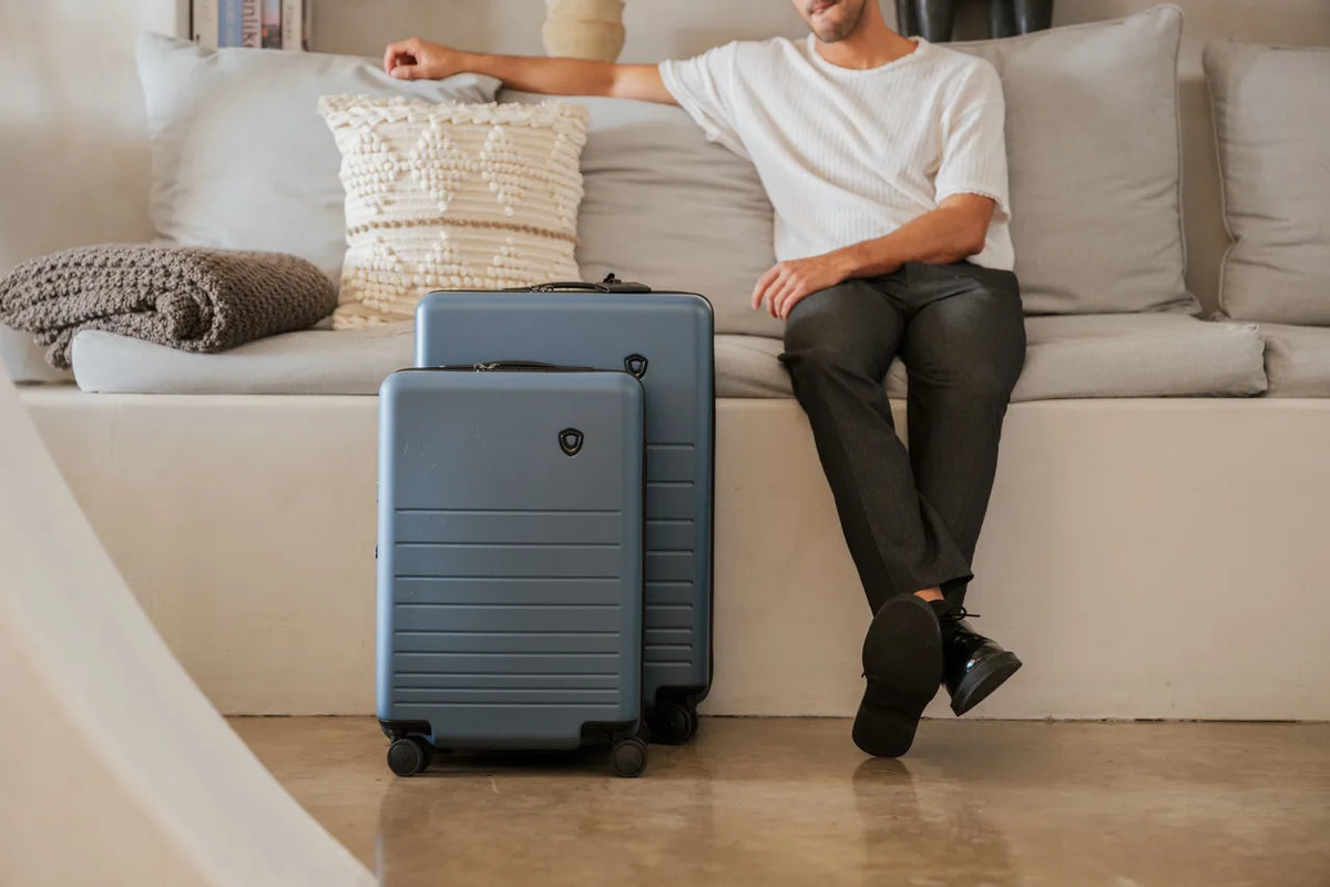 Man beside a two-piece Traveler's Choice Markham blue hardside luggage set in a modern living room
