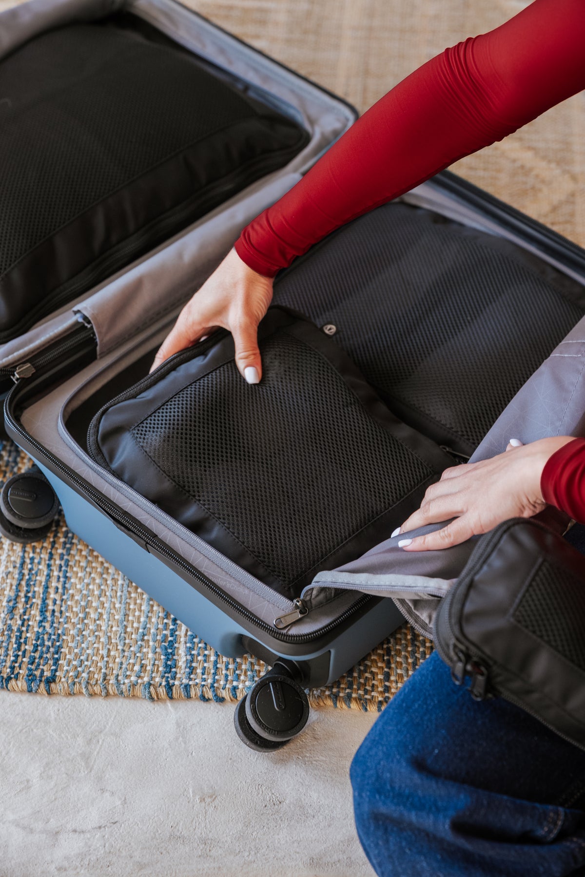 Hands opening the mesh organizer panels inside a slate blue Markham carry-on