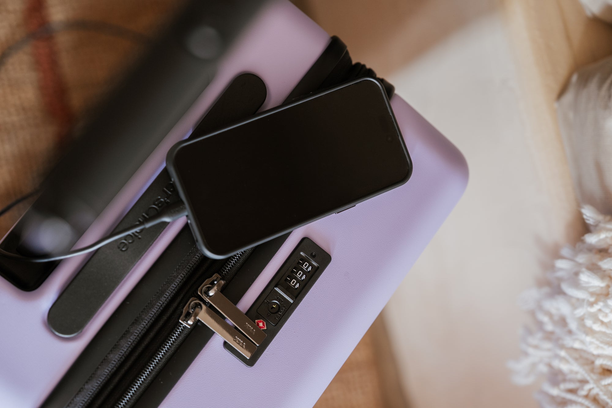 Phone lying on a lilac Markham carry-on beside its TSA combination lock