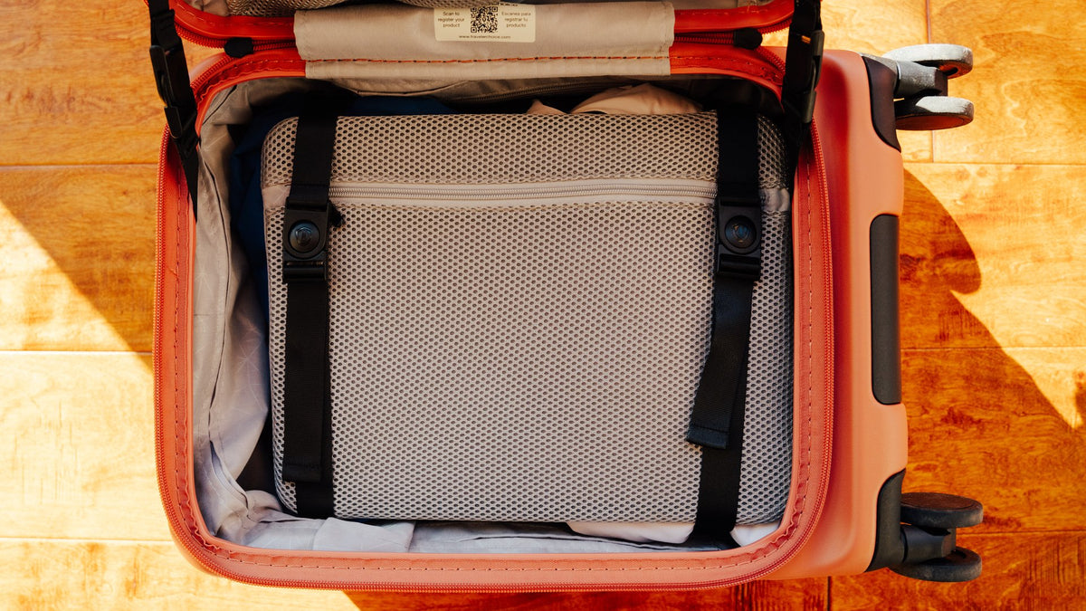 Overhead view of an open orange carry-on with a gray mesh panel and black straps holding the packed contents.