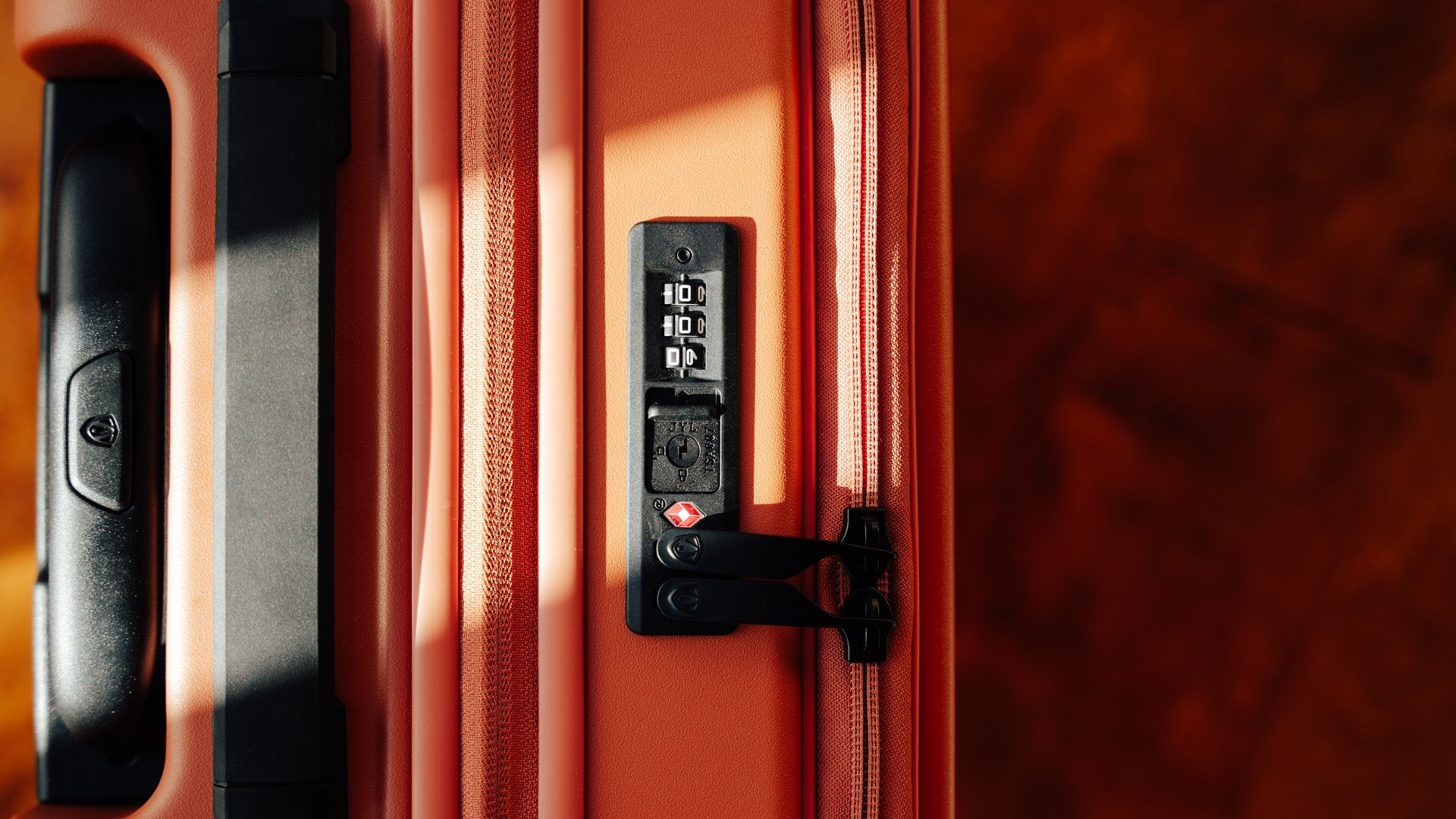 Close up of a three dial combination lock on the side of an orange hardside spinner.