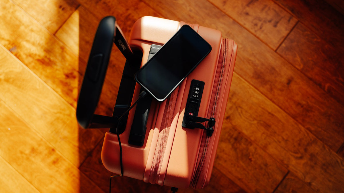 Smartphone lying on an orange hardside carry-on with the front pocket open beside the combination lock.