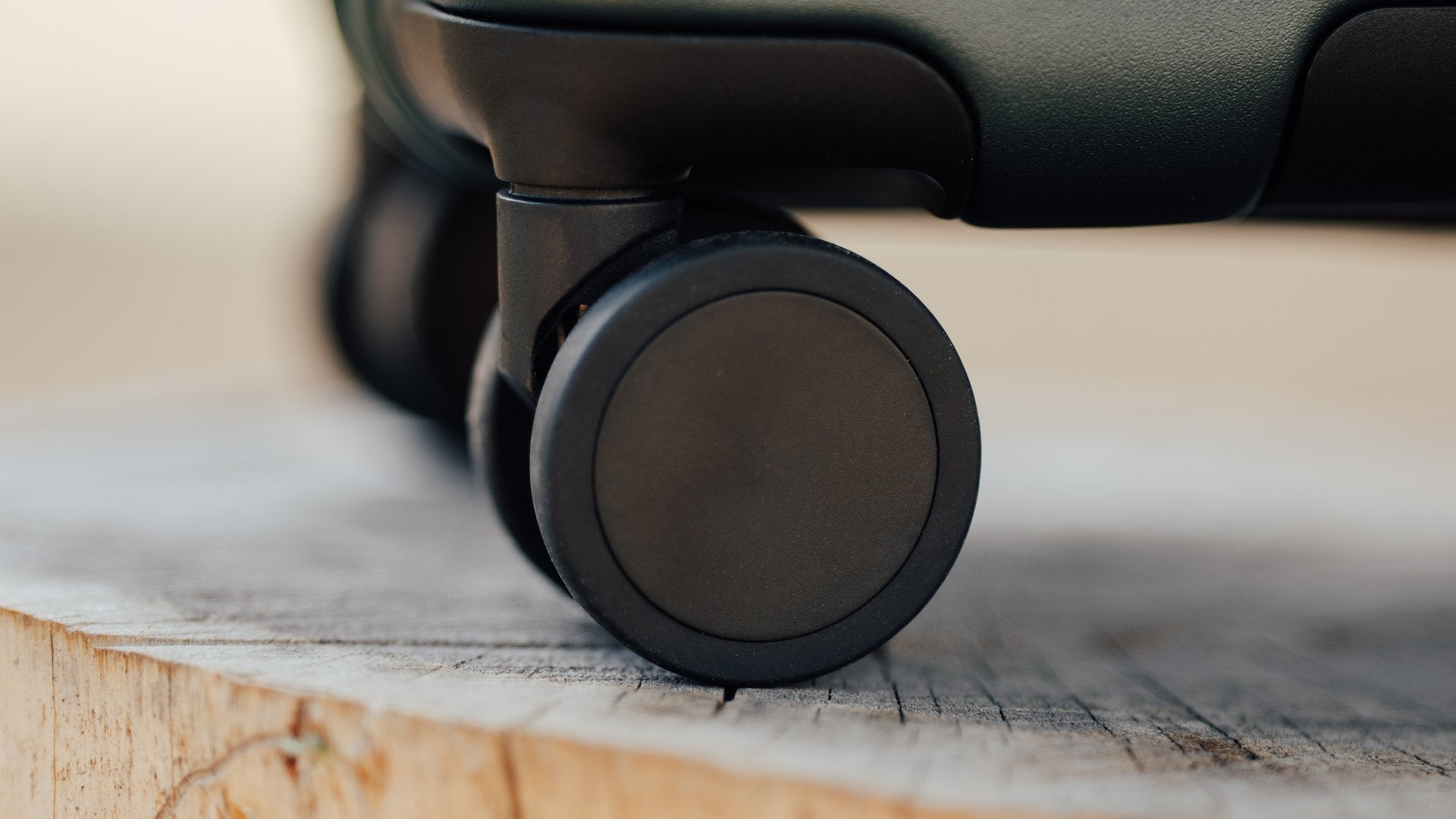 Close up of a paired spinner wheel at the corner of a dark hardside case resting on a tree stump.