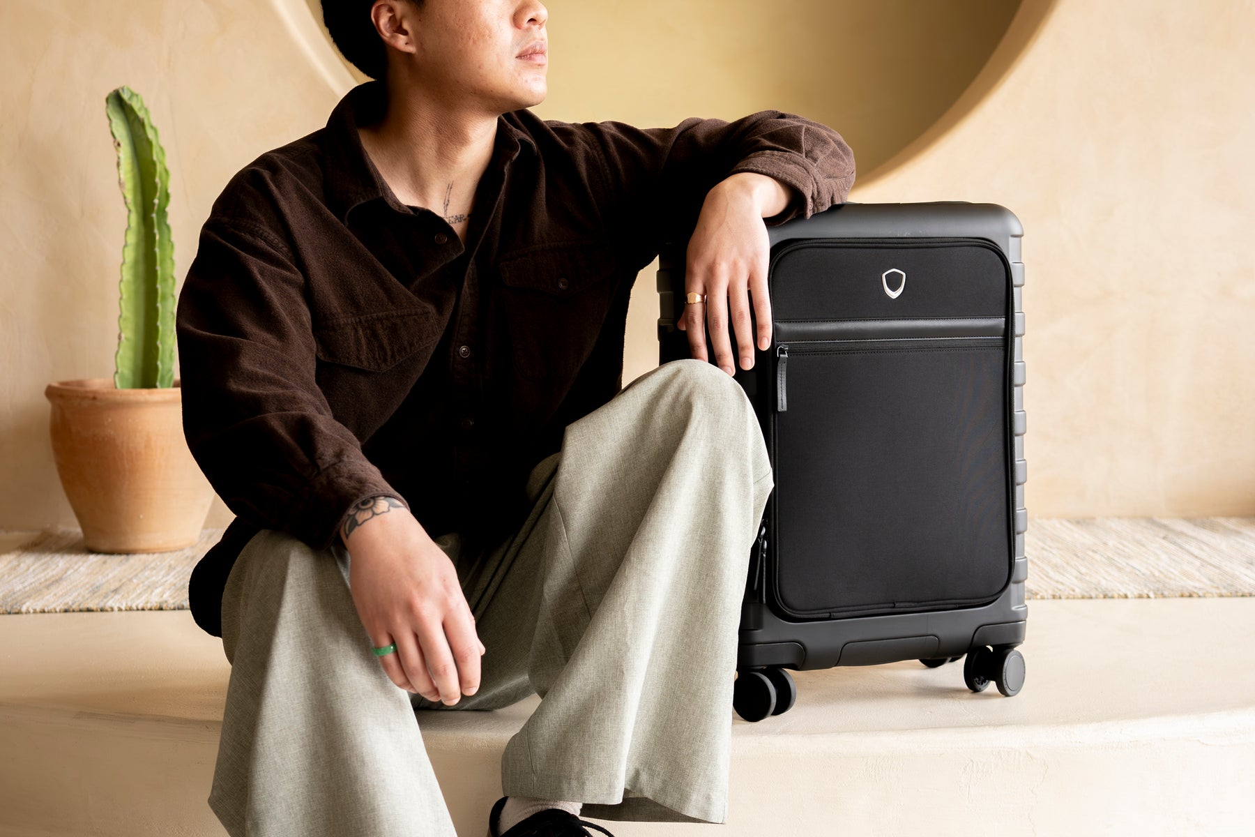 A traveler seated with an arm resting on a Traveler's Choice softside carry-on