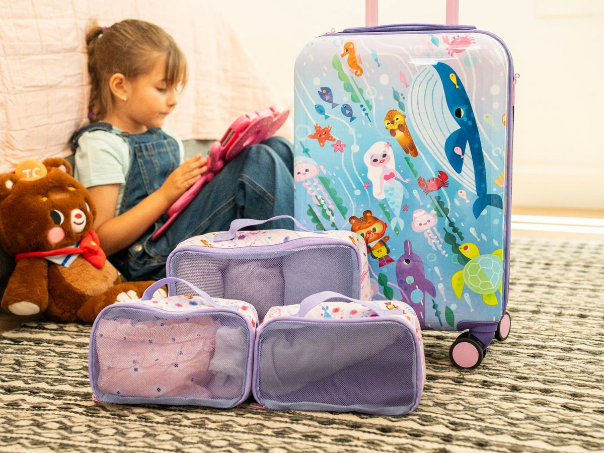 A girl sits on the floor beside the Ocean carry-on and three packed cubes.