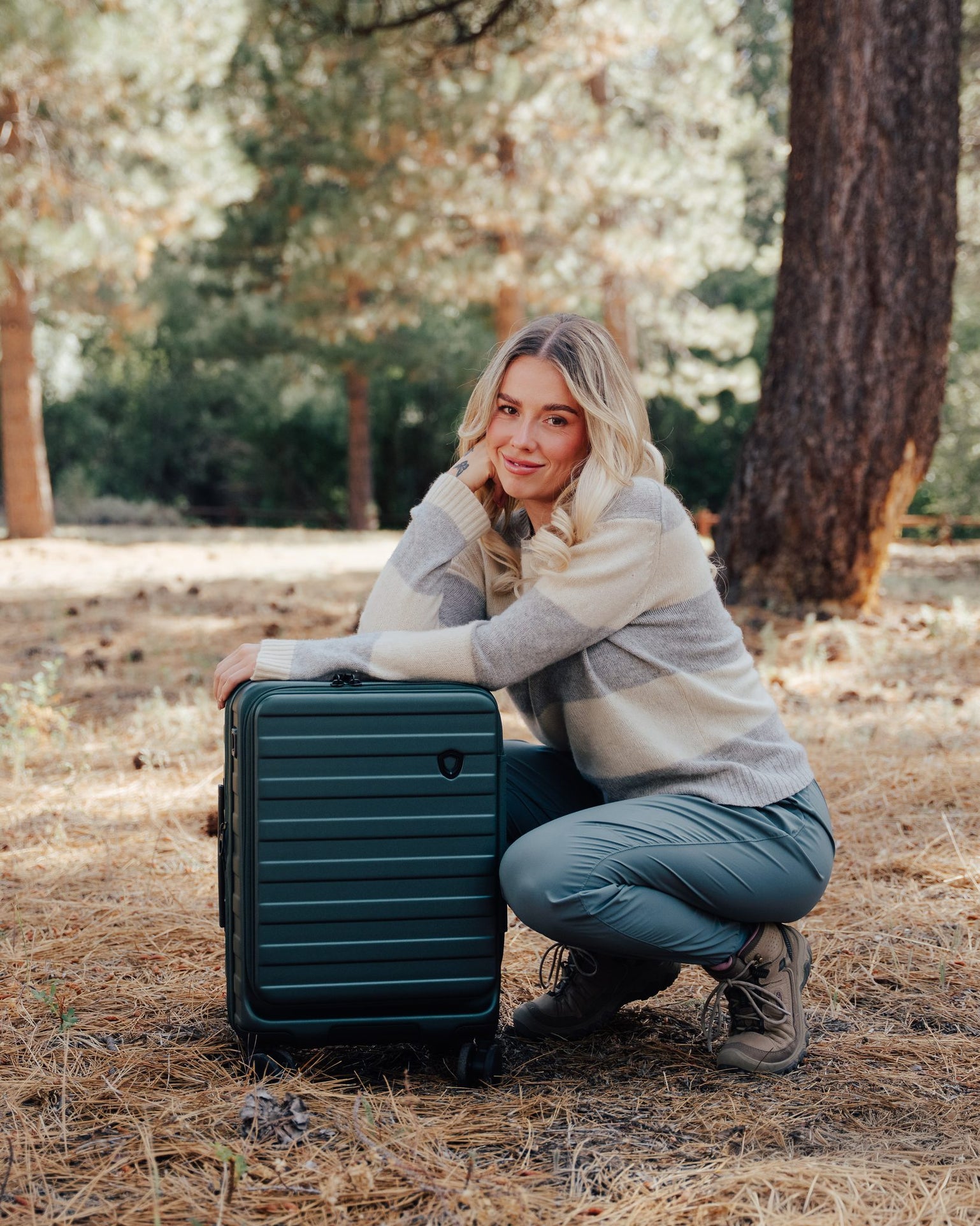 Woman kneeling beside a green Novia front-pocket carry-on in the woods