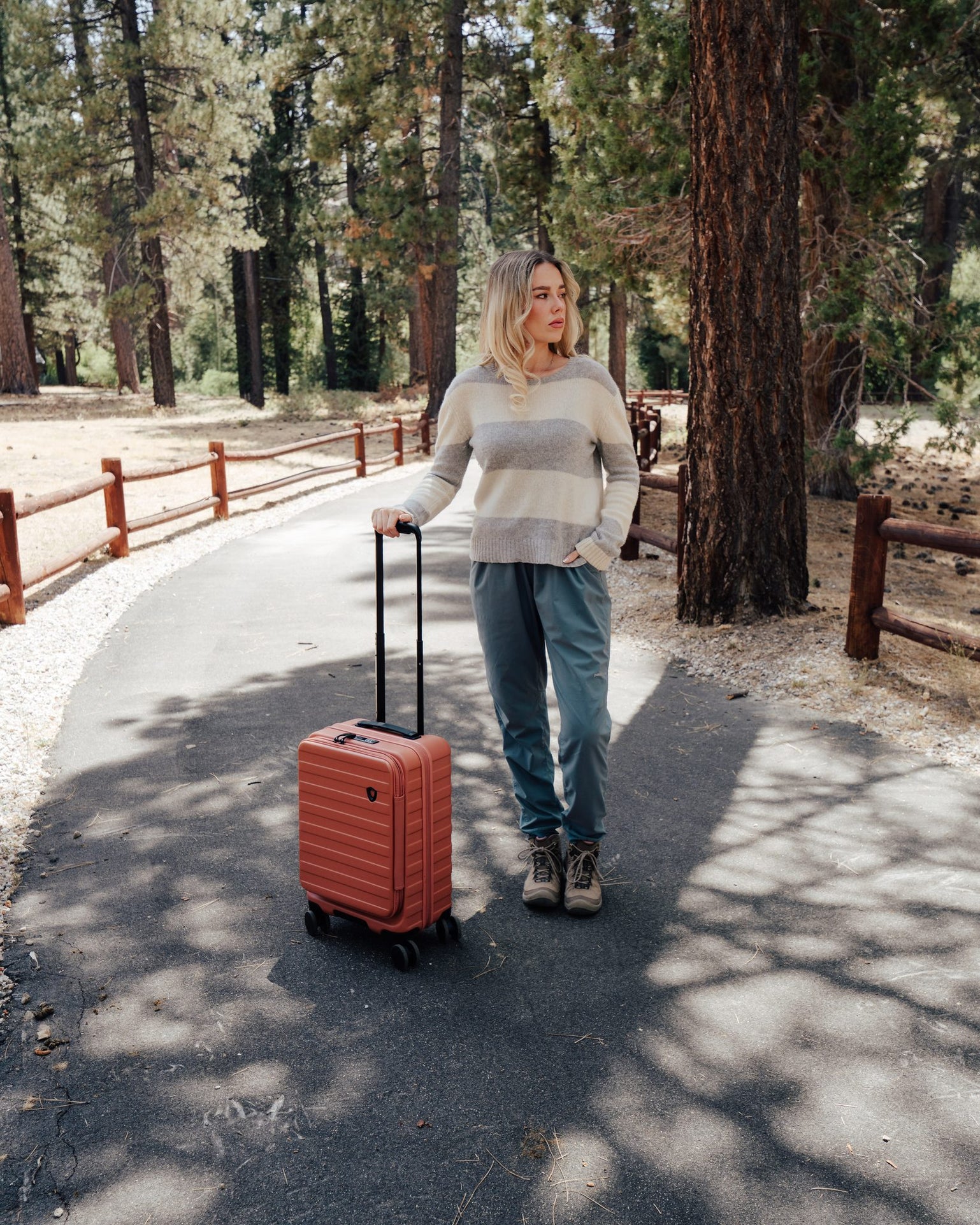 Woman rolling an orange Novia carry-on spinner along a forest path
