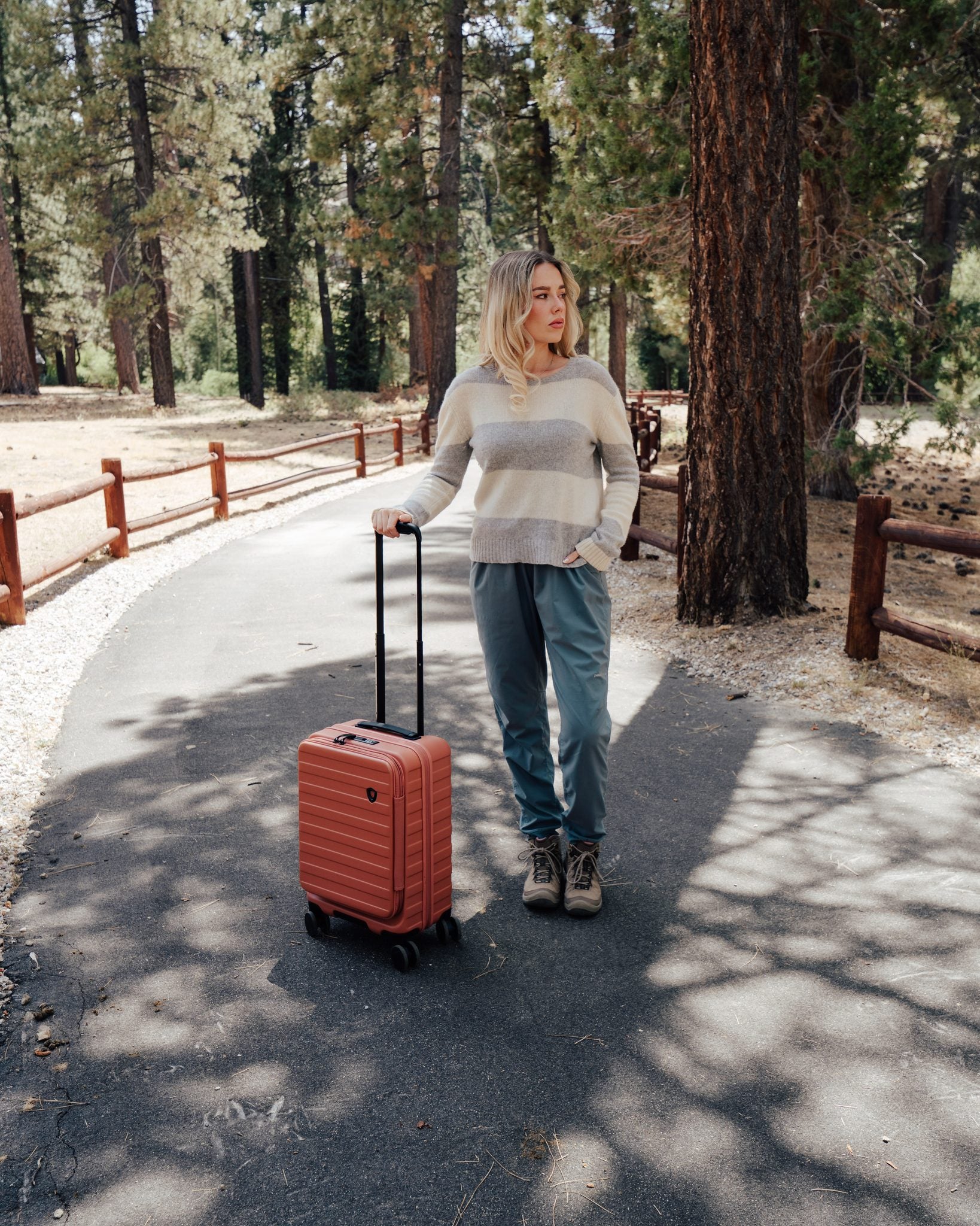 Woman rolling an orange Novia carry-on spinner along a forest path