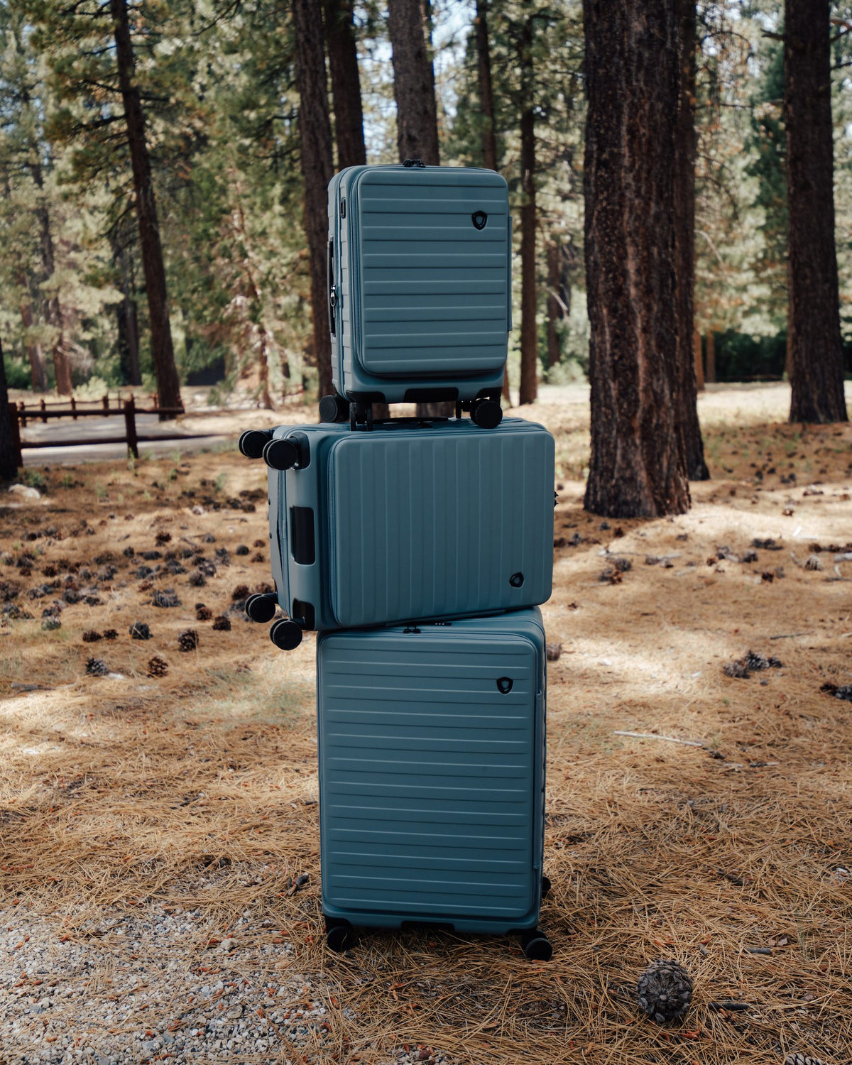 Stacked slate blue Novia hardside spinners in a pine forest clearing