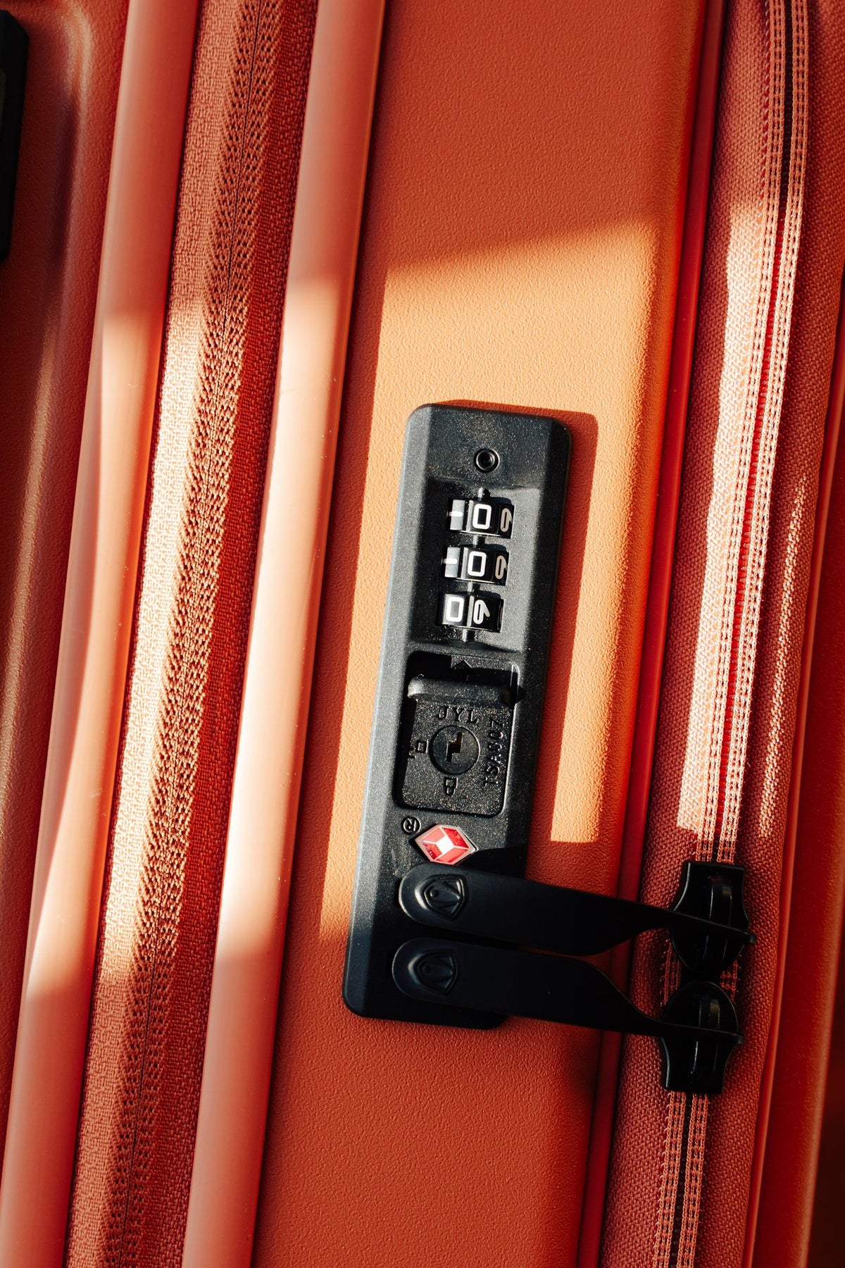 Close-up of the TSA-approved combination lock on an orange Novia spinner