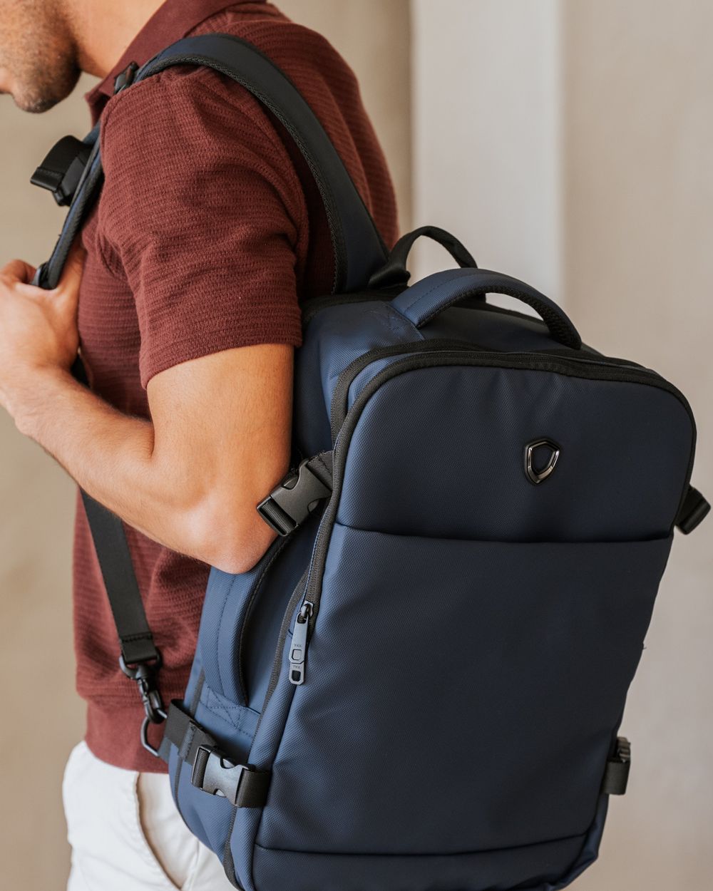 A man seen from the side wearing a navy travel backpack against a plain plaster wall