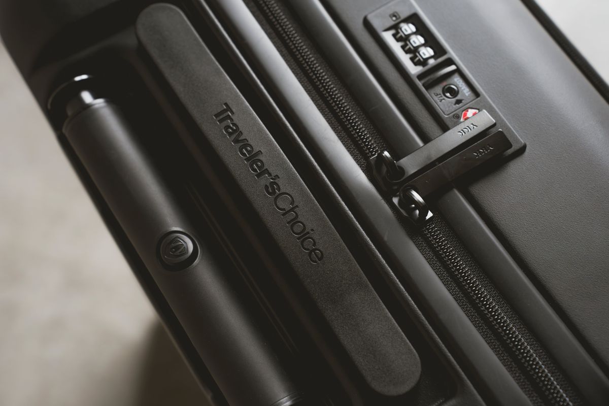 Close-up of a suitcase handle grip stamped Traveler's Choice beside a zipper pull and a three-dial combination lock