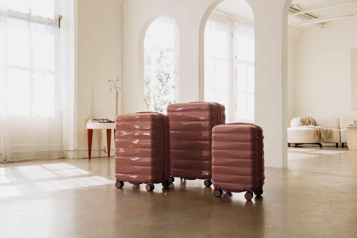 Three dusty pink hard-shell suitcases in graduated sizes standing together in a sunlit room with arched windows